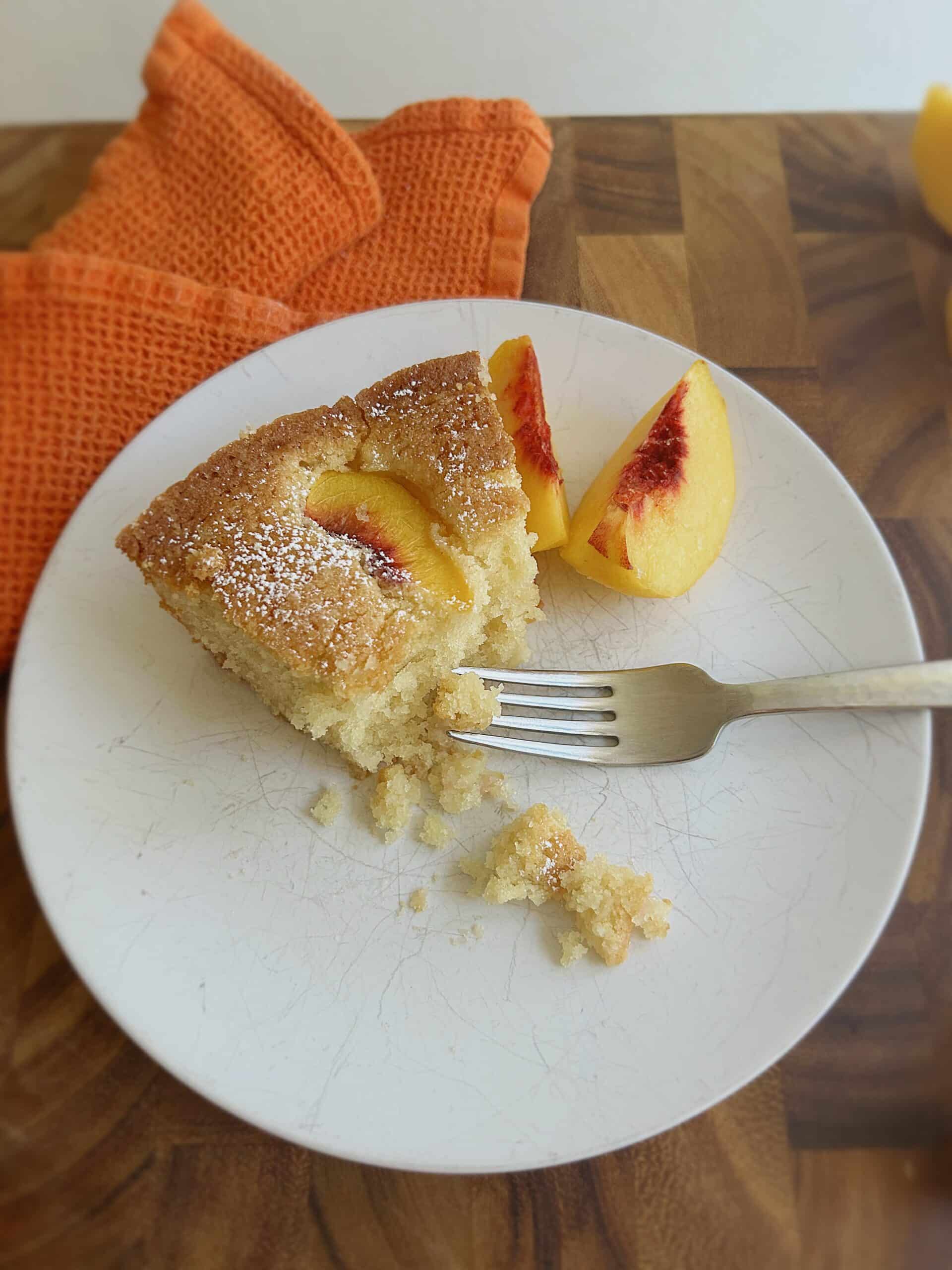 Half eaten fresh peach cake slice with crumbs and a fork.